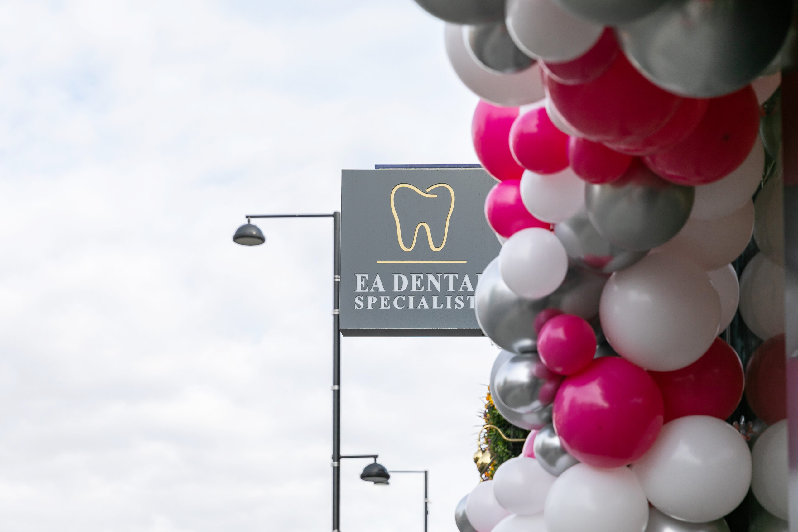 The EA Dental Specialists hanging sign outside the practice, beside a display of balloons.