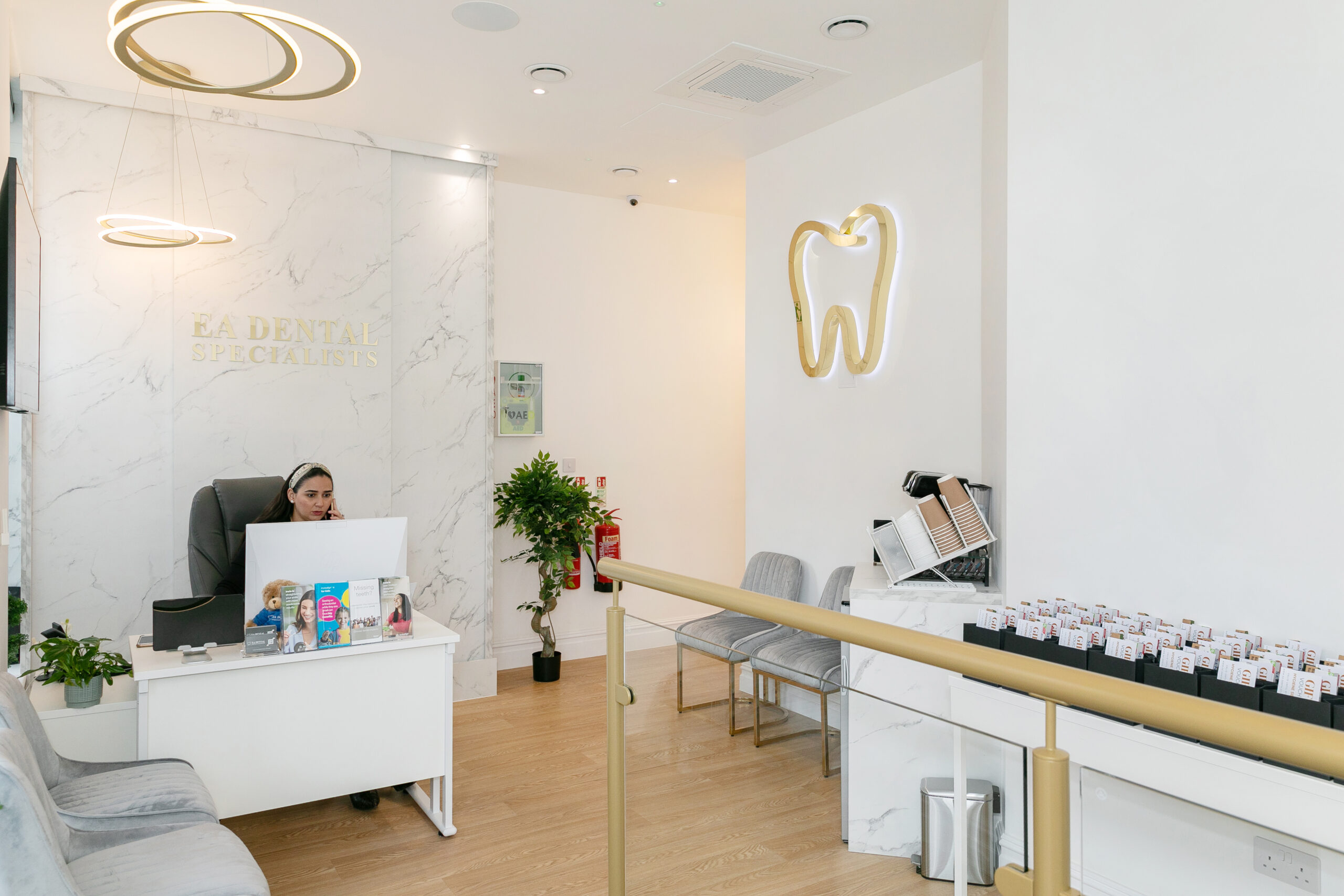 Inside EA Dental Specialists: the reception desk, gold tooth emblem, marble wall and grey waiting-area chairs.