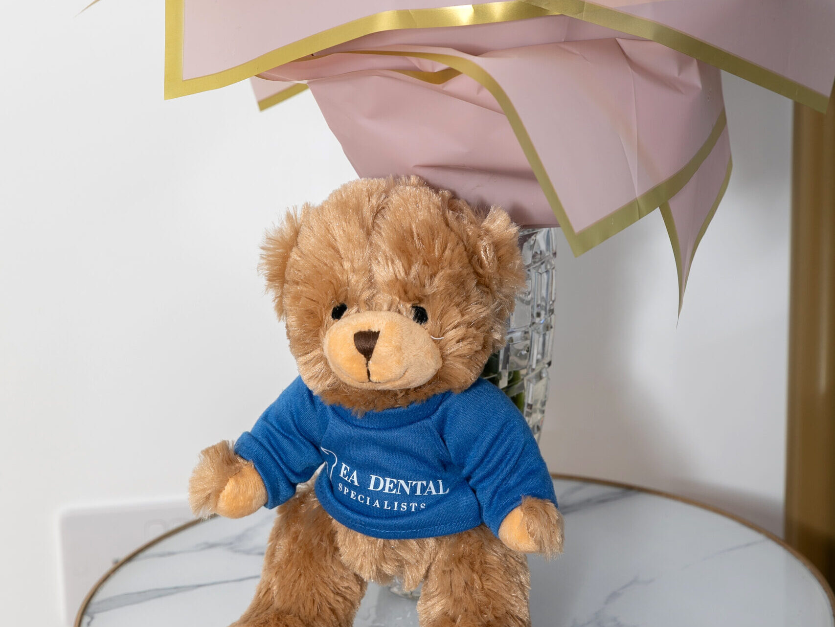 A teddy bear wearing an EA Dental Specialists shirt beside flowers at the practice.