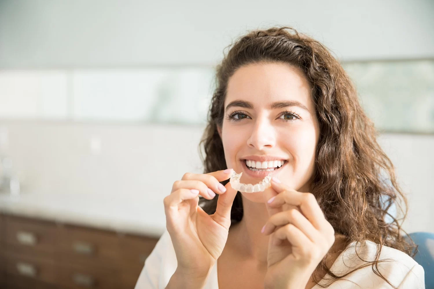 A woman holding a clear dental aligner in front of her smile.