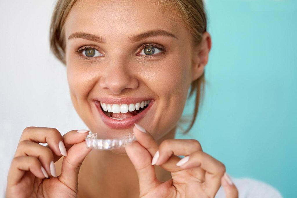 A smiling woman holding a transparent dental aligner with both hands.